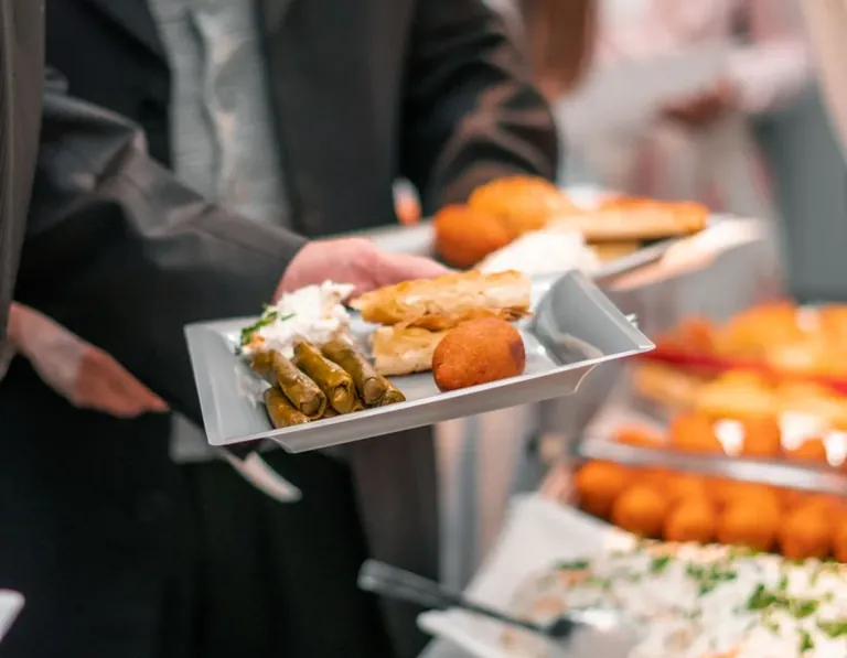 Официант в тёмном костюме держит поднос с закусками у фуршетного стола