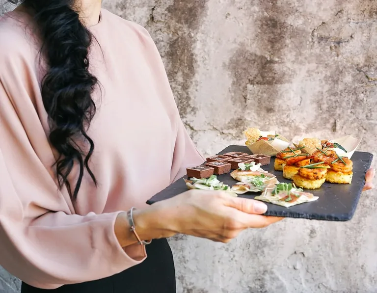 Женщина несёт сланцевую доску с закусками